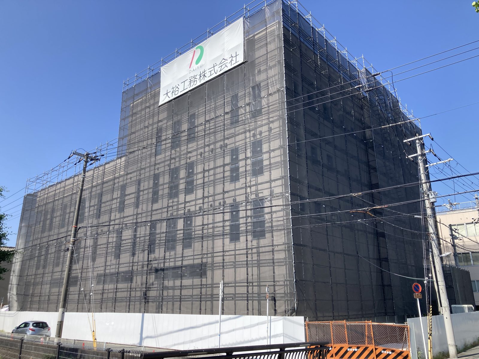 外壁工事。足場に養生シートを掛け、外壁パネルを施工中の建物